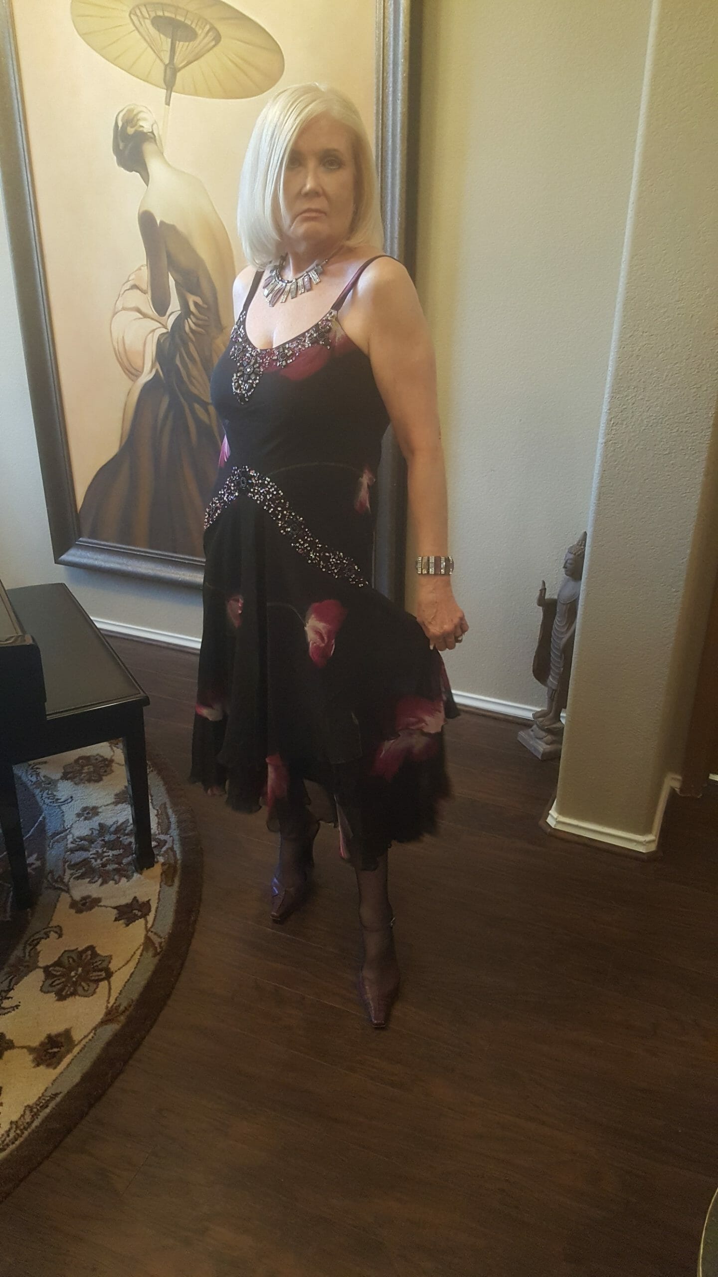 Side view of a Midnight Velvet customer by a large painting, in a black and magenta floral print dress.