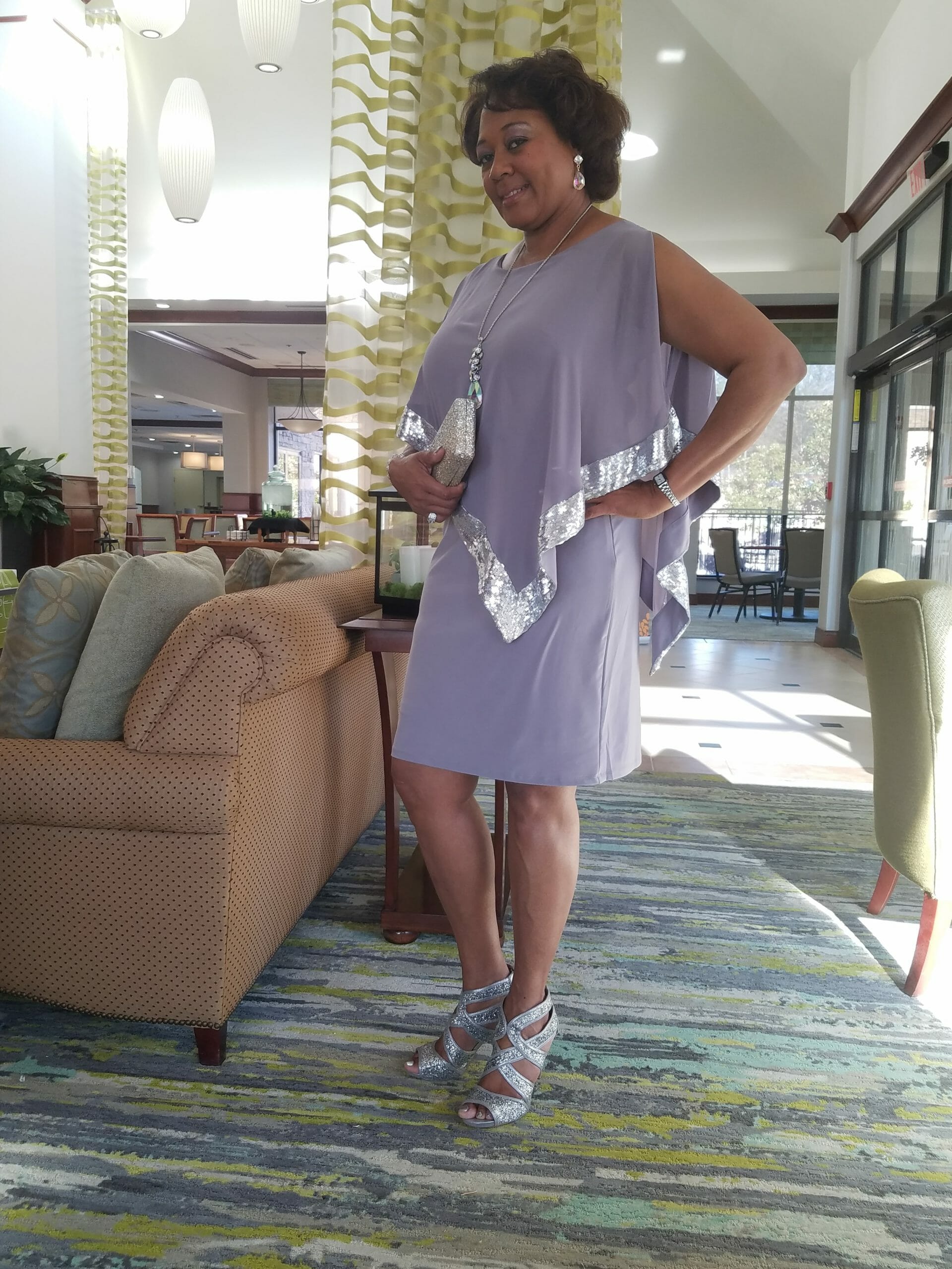 Side view of a Midnight Velvet customer, in a lavender dress with silver trim on the cape-like top, and silver sandals.