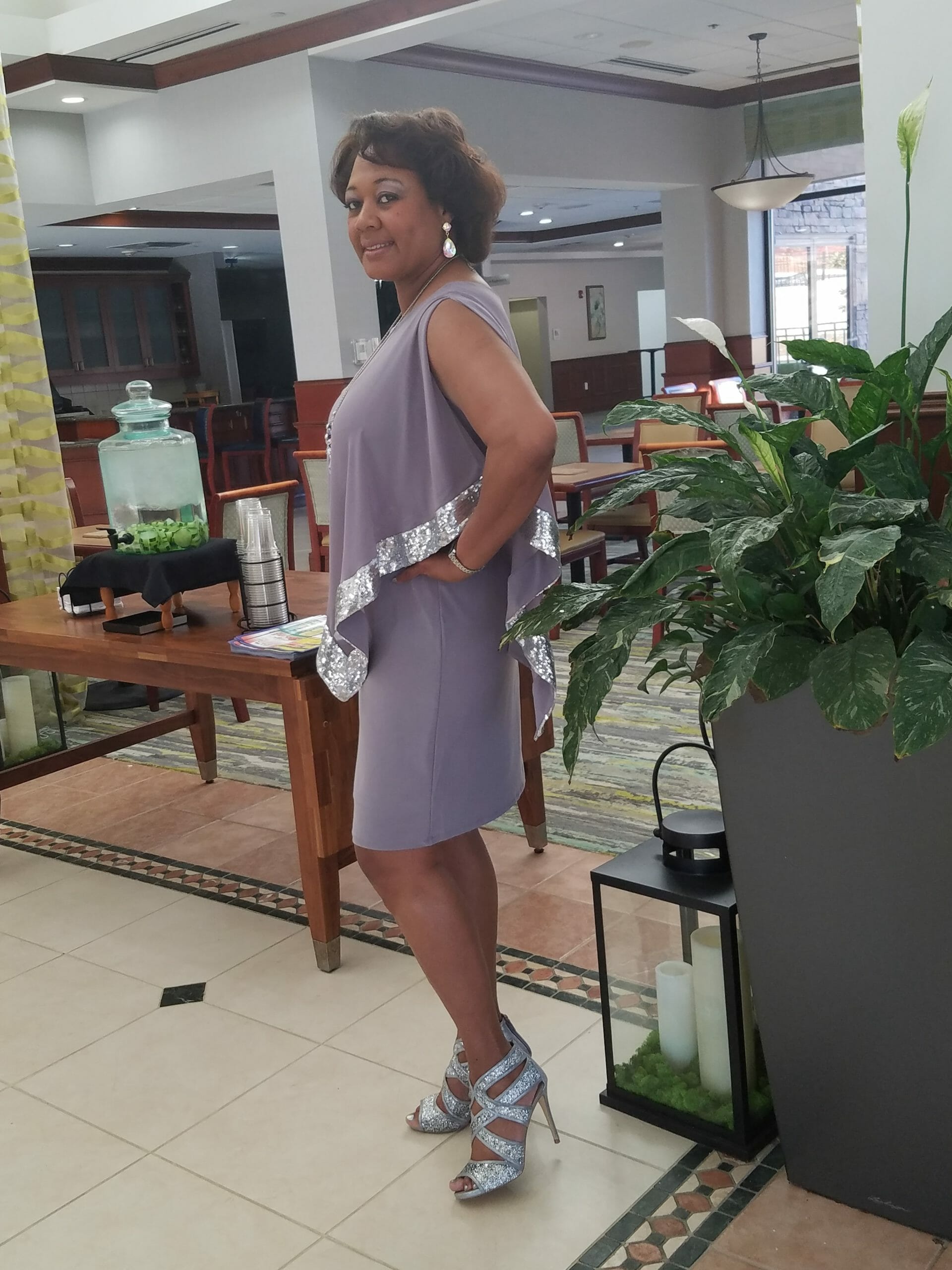 Side view of a Midnight Velvet customer, in a lavender dress with silver trim on the cape-like top, and silver sandals.