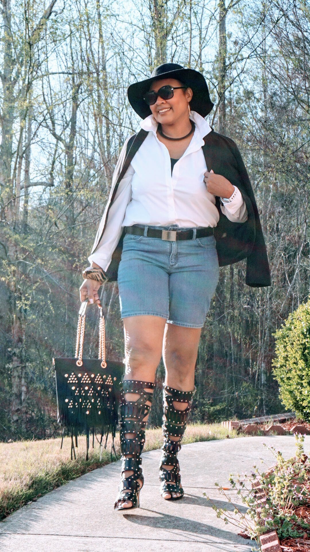 A smiling Midnight Velvet customer, in a white shirt, black jacket, jean shorts, black studded boots, and brimmed black hat.
