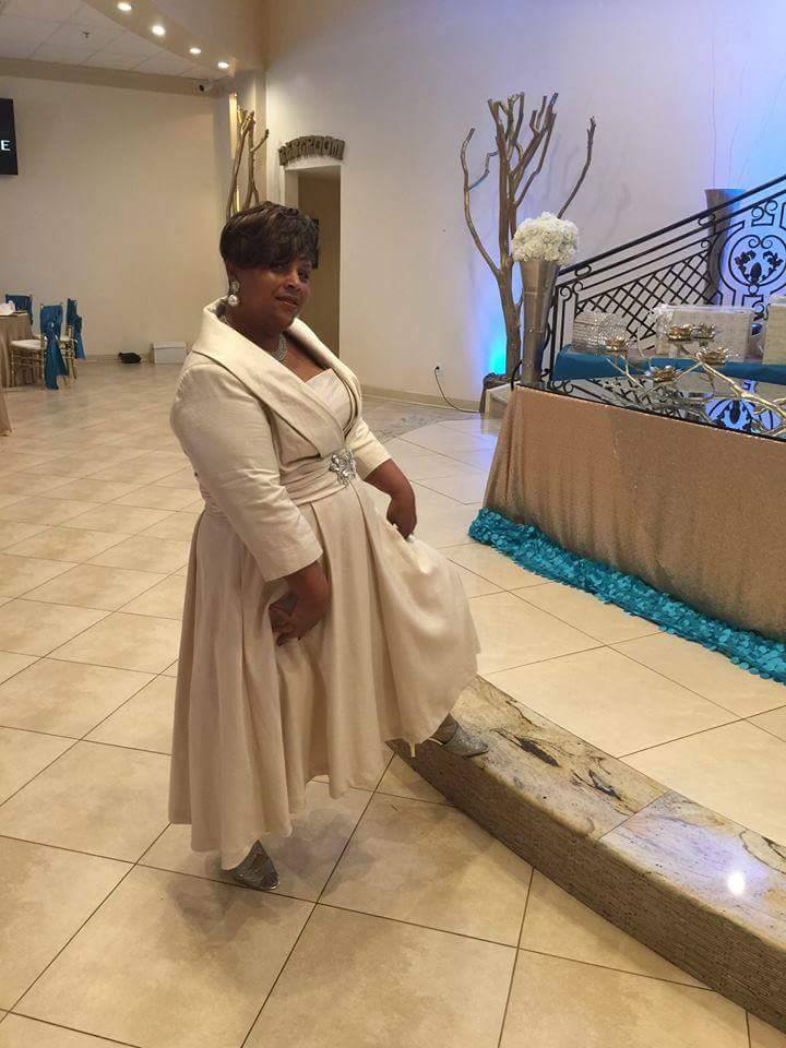 A Midnight Velvet customer at an event, in a formal beige jacket dress with a full skirt and a crystal front clasp.