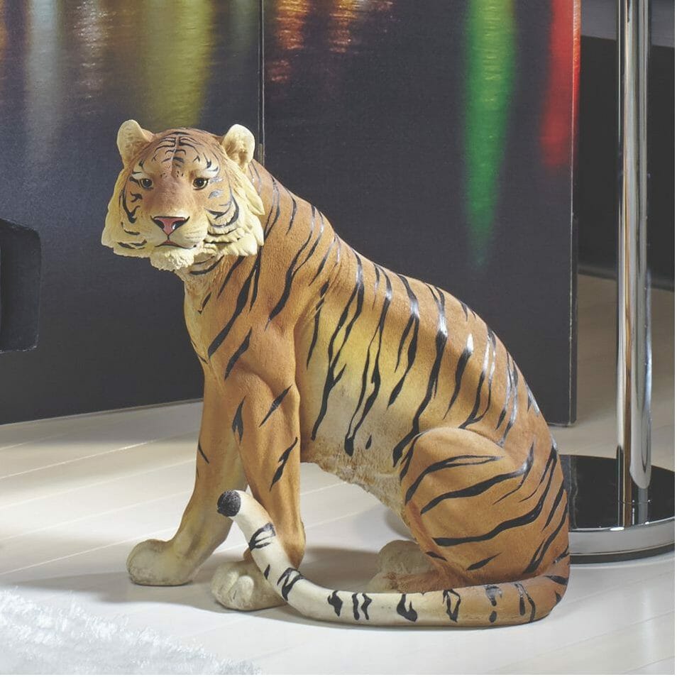 A life-like seated tiger statue on a floor next to a multicolor screen.