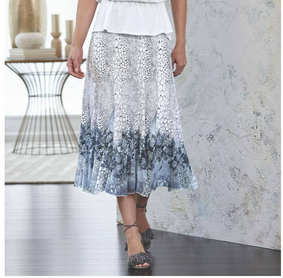 Lower half of a woman wearing a full skirt in a white and black reptile print with a blue floral design at the bottom.