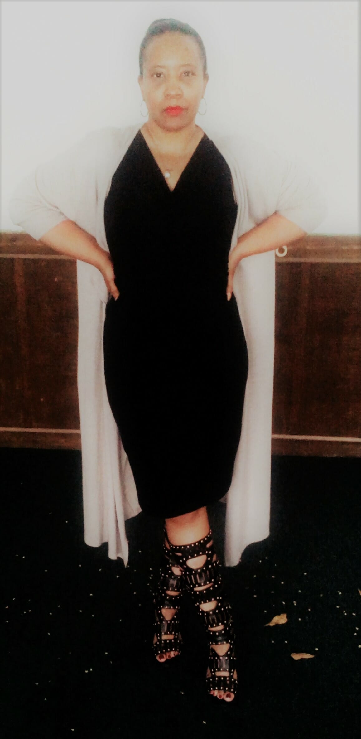 A Midnight Velvet customer in a black V-neck dress, long white cardigan, and tall black studded boots.