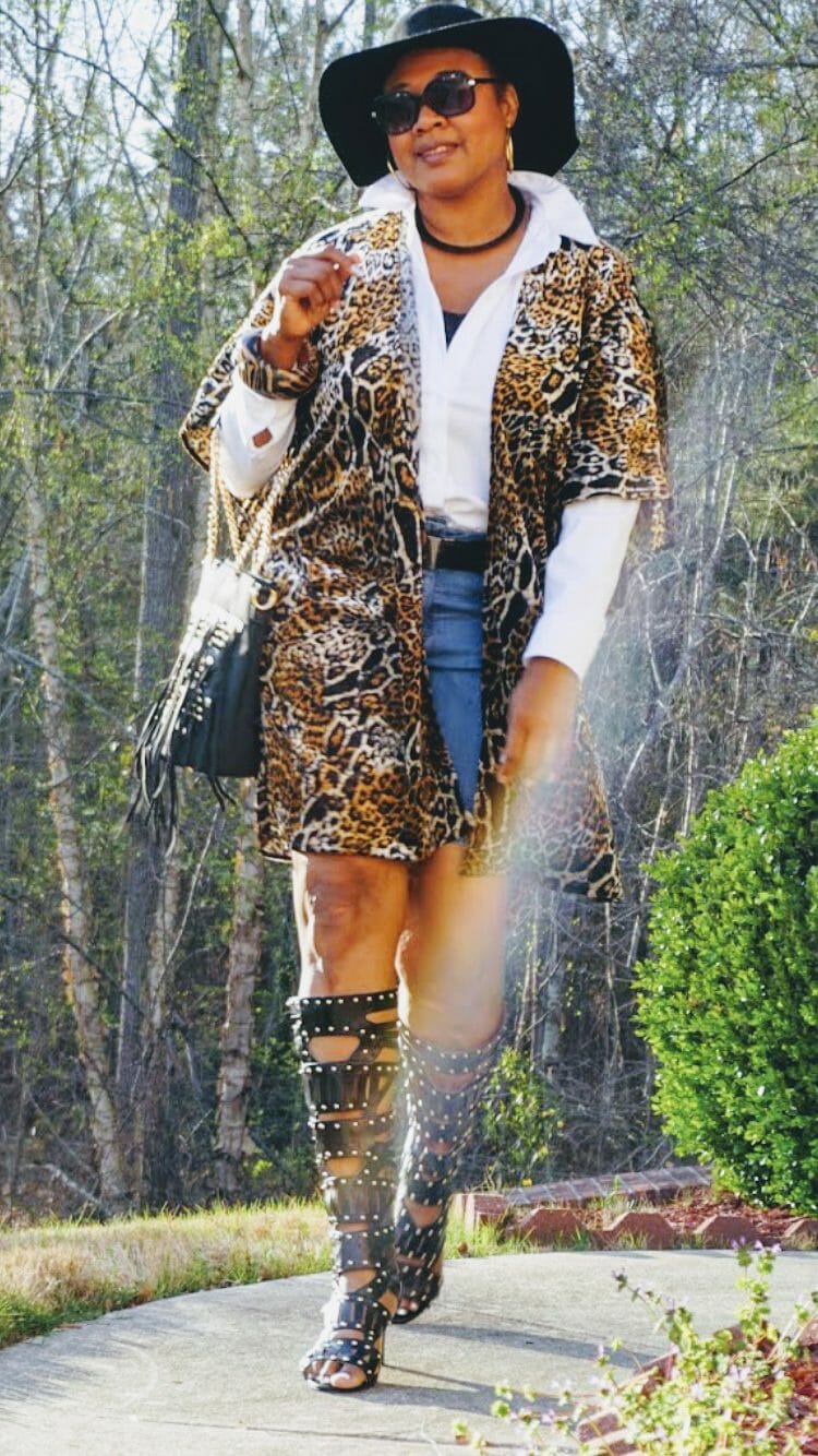 A Midnight Velvet customer in sunglasses, a shirt and animal print cardigan, black studded boots and bag, and a black hat.