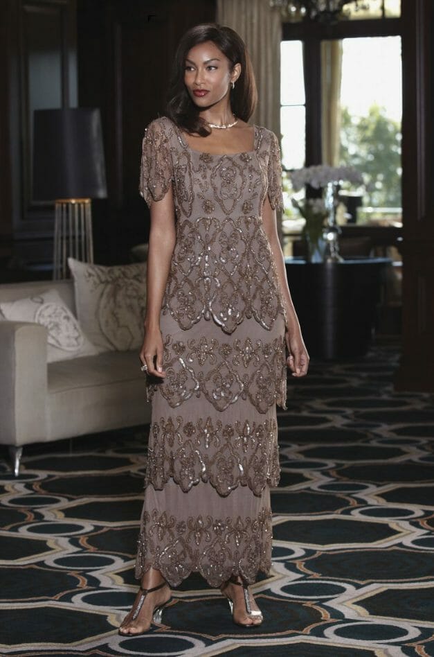 An African-American woman in a heavily beaded, four-tier, long taupe dress, with matching heeled sandals.