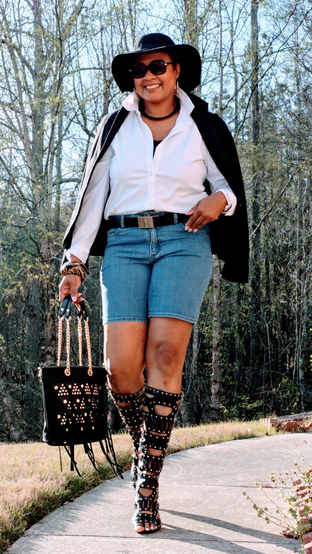 A Midnight Velvet customer in sunglasses, a shirt and black jacket, black studded boots and bag, and a black hat.