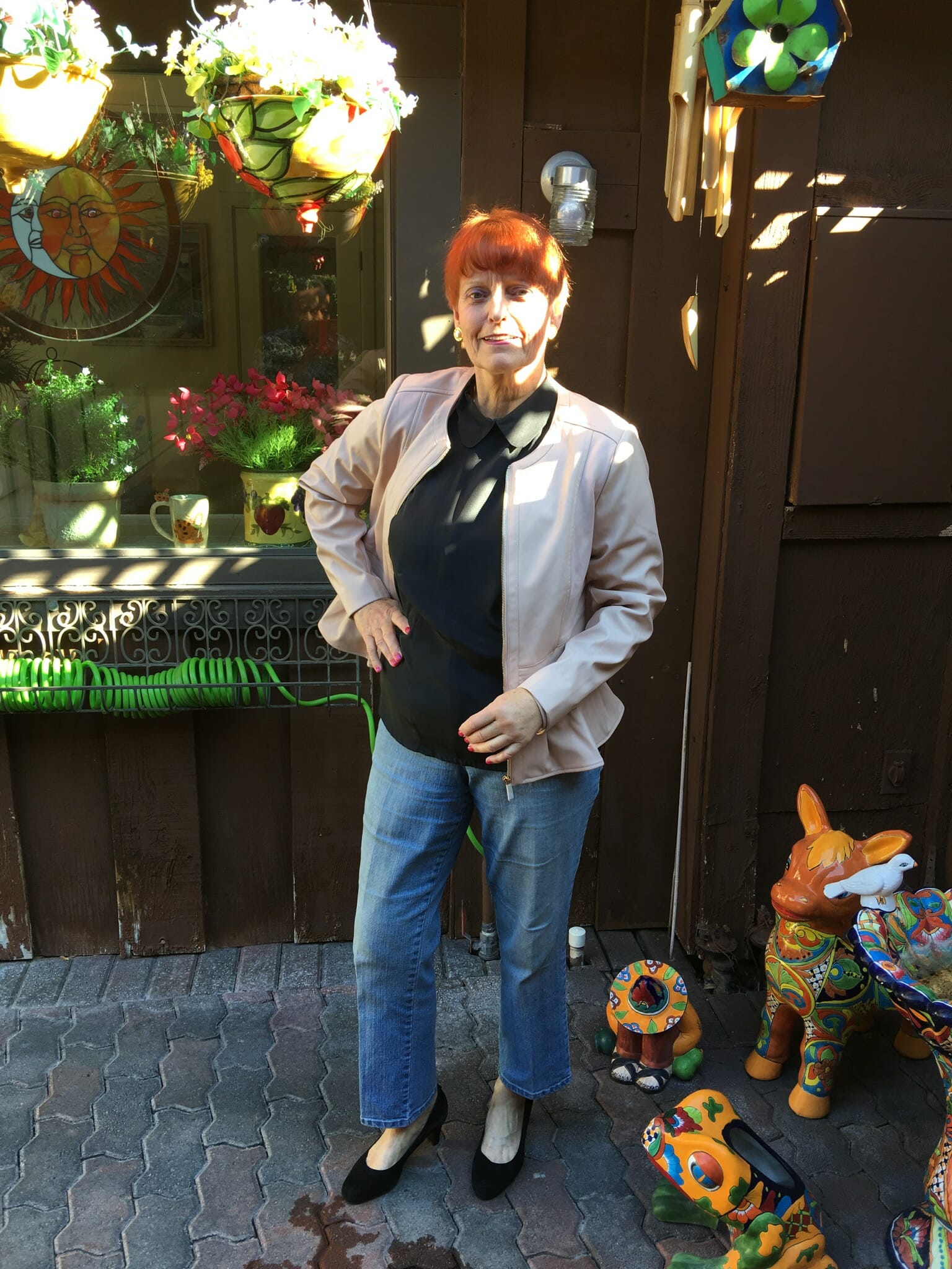 A Midnight Velvet customer on a patio with Mexican pottery, in a blush peplum jacket, gray top, and denim jeans.