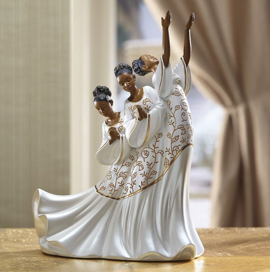 A figurine of three praying and praising African-American women in a long white and gold gown.