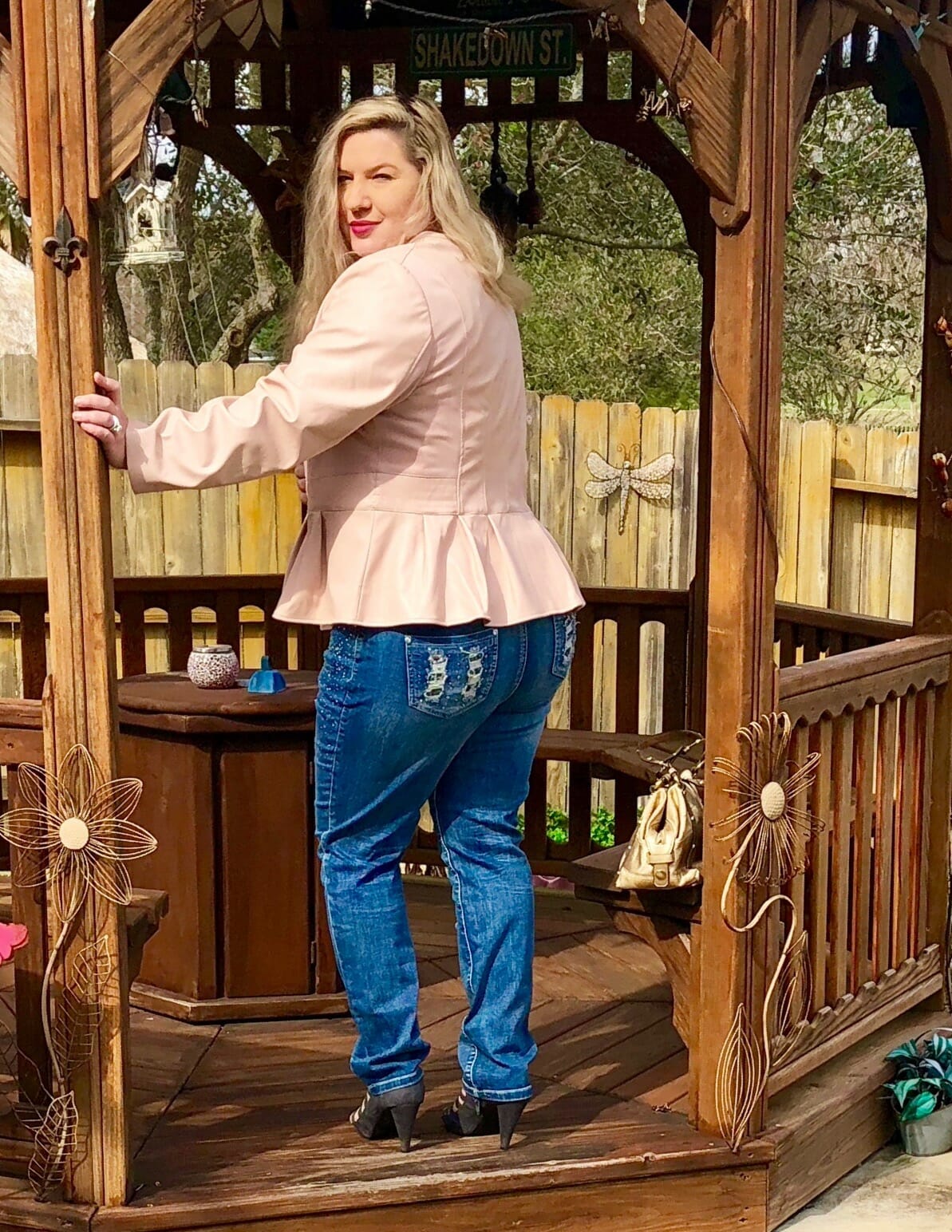 Back view of a Midnight Velvet customer in a gazebo, wearing a blush peplum jacket and jeans with embroidered pockets.