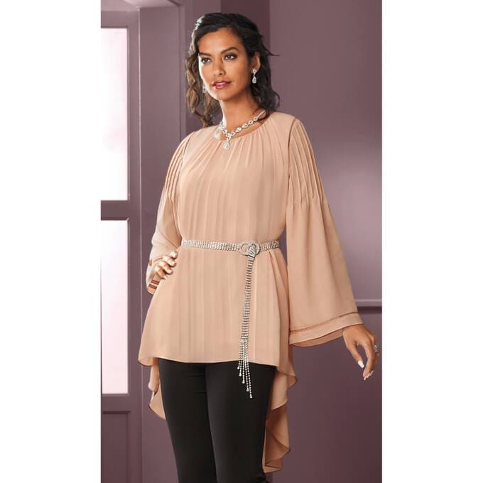 Elegant woman in a pleated beige top with a jeweled belt, paired with black pants, posing against a soft purple background.