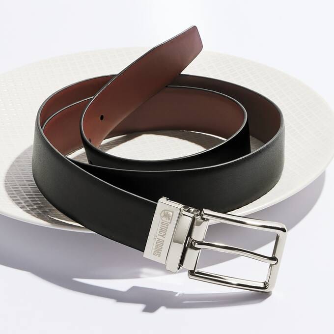 A black leather belt with a silver buckle, elegantly displayed on a textured white plate.