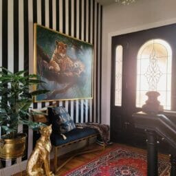 Golden Leopard Statue sitting in entryway of a home, in front of black and white striped wall on a red rug