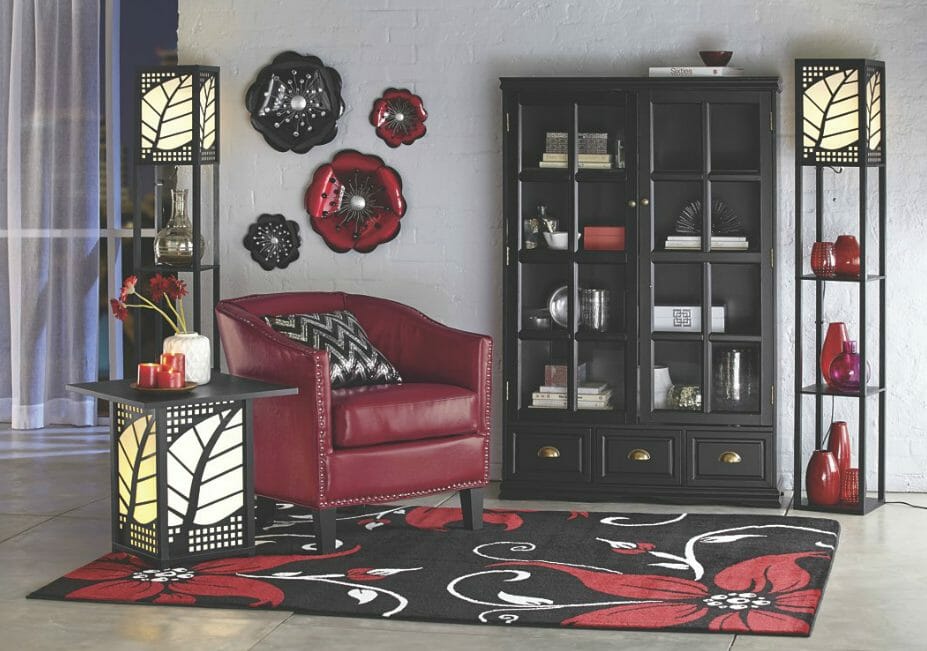 Room setting in red, black and white: a chair, pillow, floral rug, two etageres, glass door bookcase, and flowers wall art.