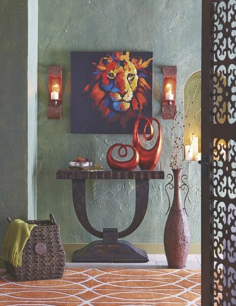An eclectic area with modern brown console, colorful lion head wall art, woven basket with throw, two sconces and tall urn.