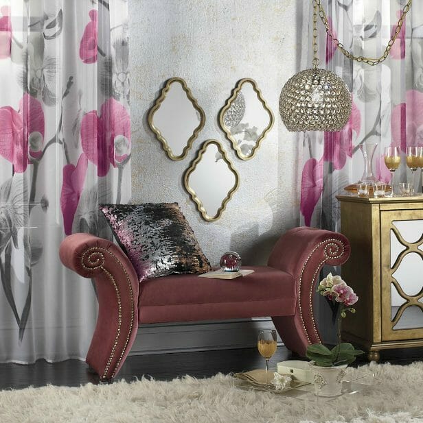 A mauve scroll bench, white, gray and rose floral curtains, three gold framed mirrors, white shag rug and a gold console.