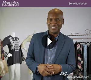 A video about a smiling black designer man in a suit jacket, next to a dressed mannequin and a rack of clothing.
