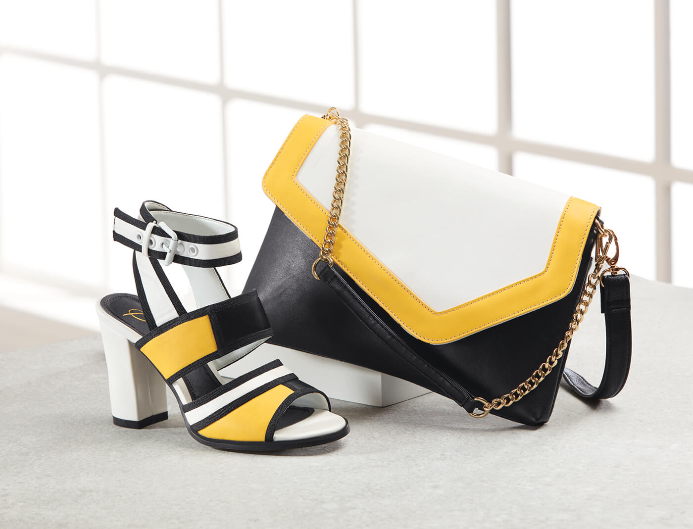A colorblock envelope clutch in white, black and yellow, with a matching ankle strap sandal with a chunky heel.