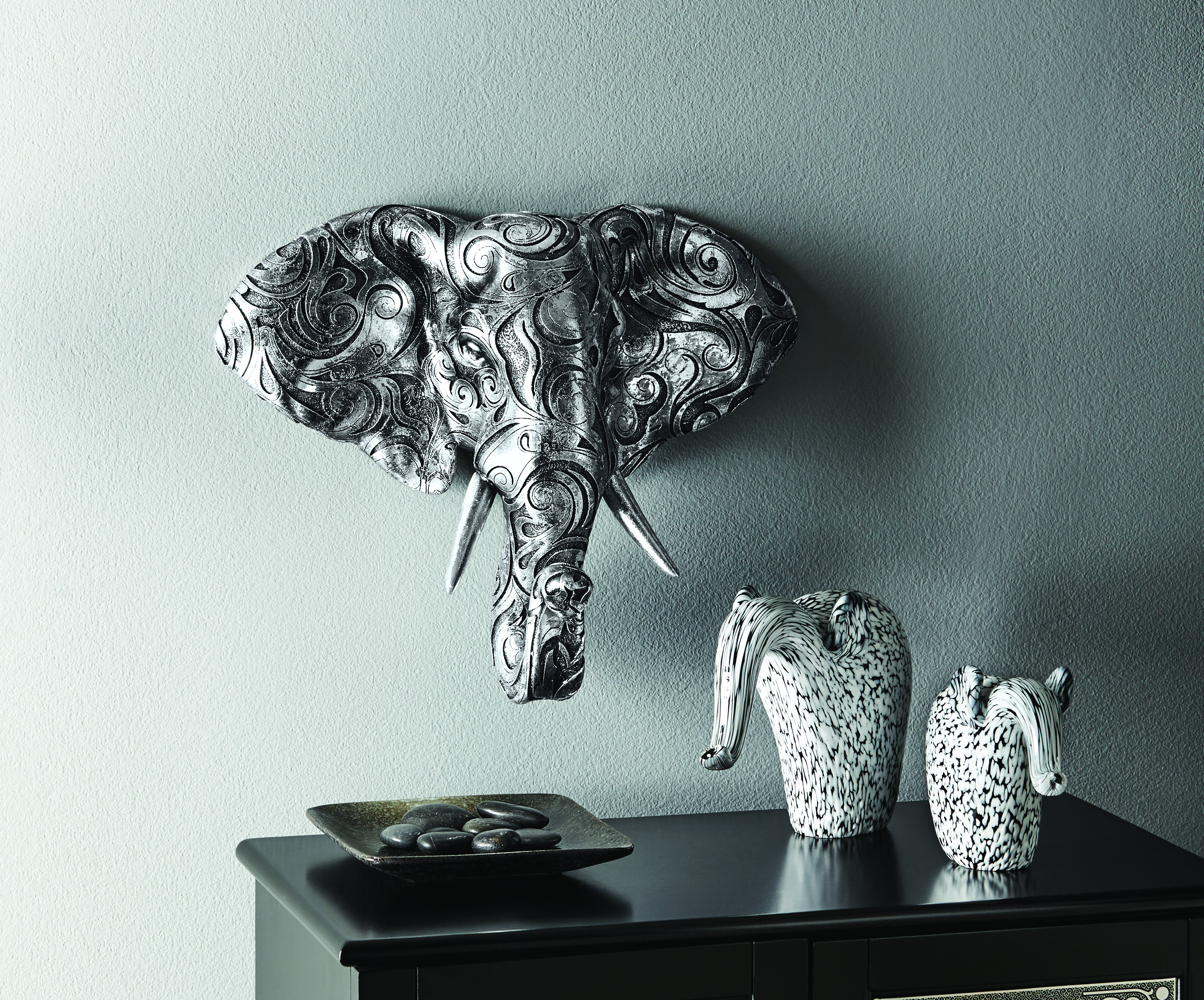A black and silver swirl elephant head wall plaque and a set of two black and white elephant figurines on a console.