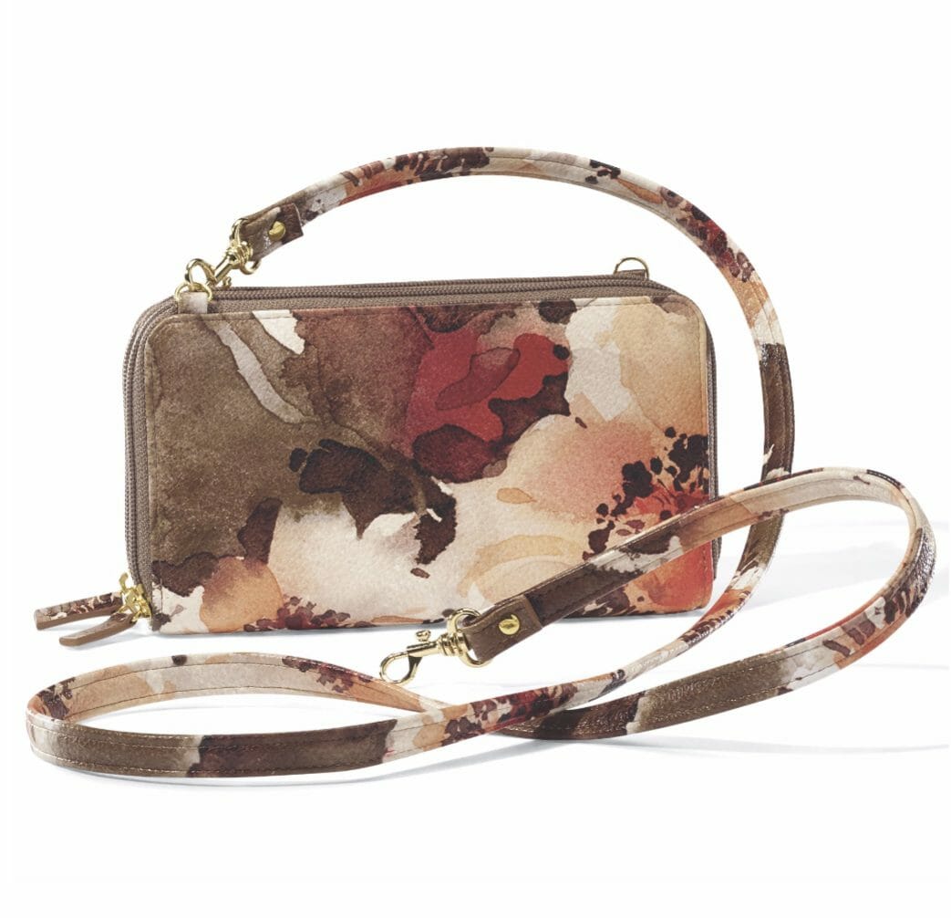 A zippered clutch in a burgundy, ivory and brown floral watercolor design with a matching floral shoulder strap.