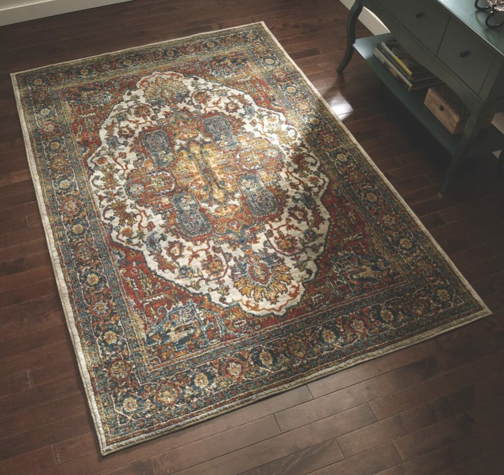 An Oriental style rug with a medallion design in ivory, rust, navy, moss and gold, placed on a wood floor by a moss console.