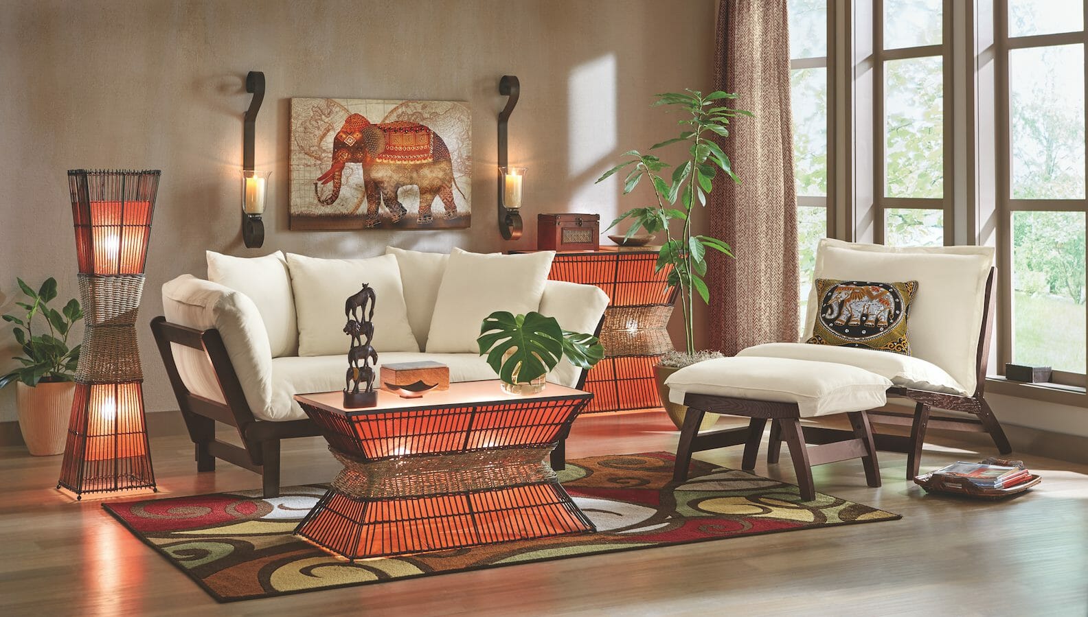 An Afrocentric living room with an ivory futon and chair, lit orange and wicker tables, an elephant wall canvas and figurines.