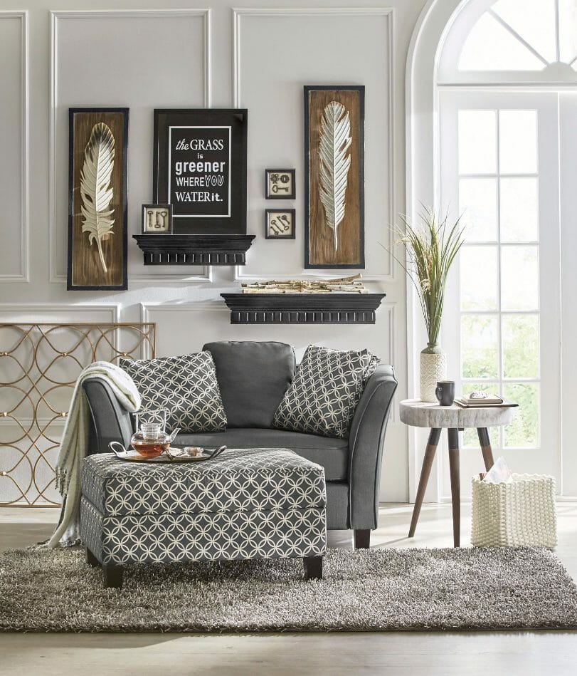 Room setting in white, gray and browns, with a love seat, ottoman, shag rug, and two large feathers next to a framed quote.