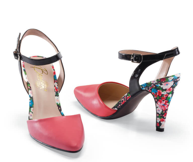 A coral pump with a black ankle strap and a floral print on the sides and heel of the shoe.