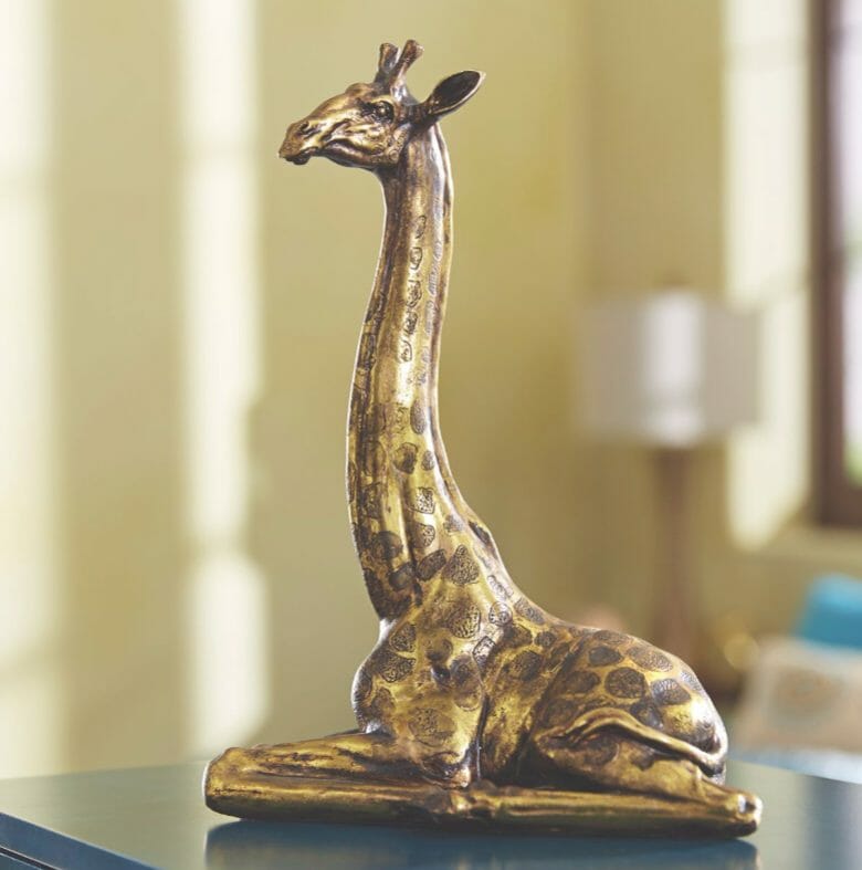A brass and brown figurine of a sitting giraffe.