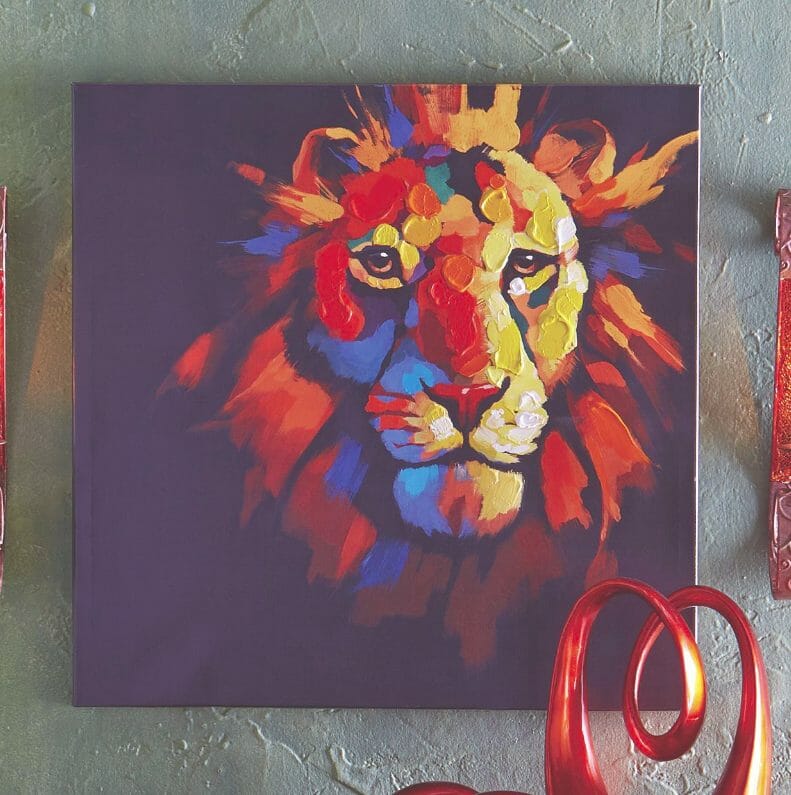 A colorful canvas of a lion's head on a black background, hanging on a textured wall.