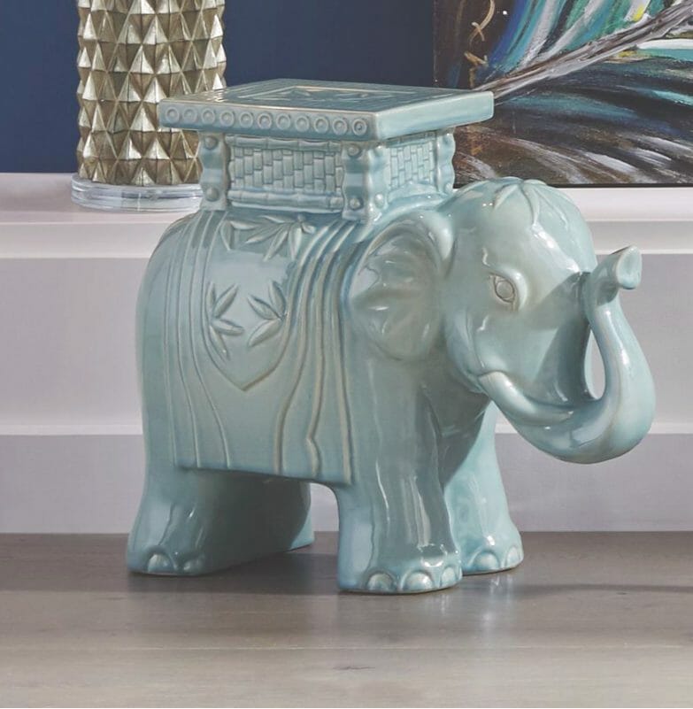 A light blue and white glazed elephant figurine with a raised trunk, saddle blanket and platform saddle.