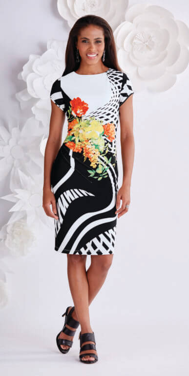 A brown woman wearing a short-sleeve black and white graphic print dress, with a splash of orange and yellow flowers.