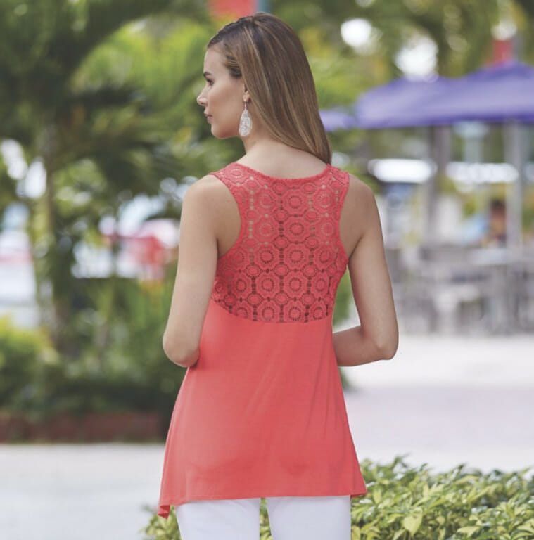 Back view of a woman outdoors, wearing a coral lace back sleeveless top, white drop earrings, and white pant.