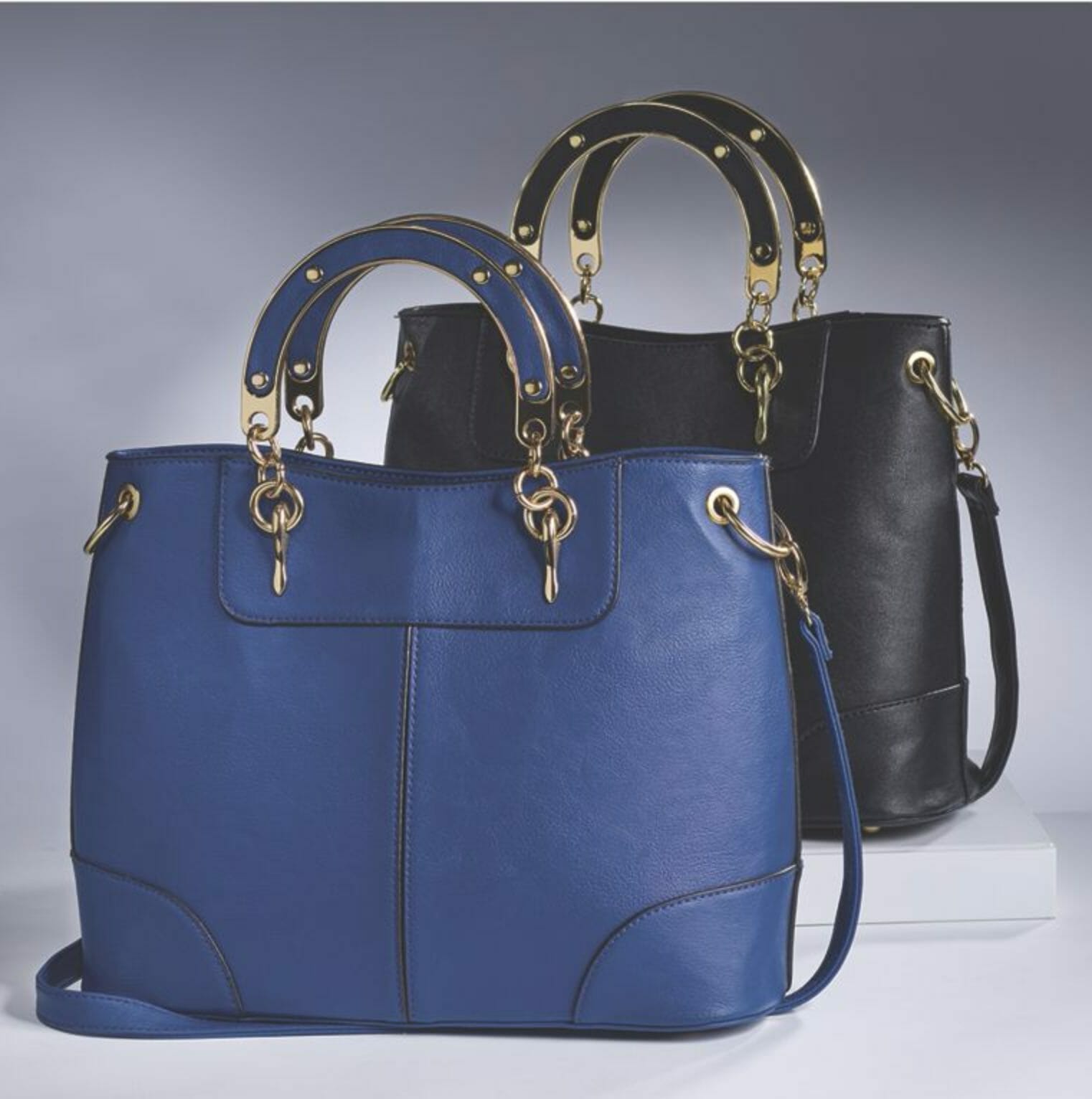 Two faux leather satchel bags with gold curved metal handles with gold studs, one in royal blue and one in black.
