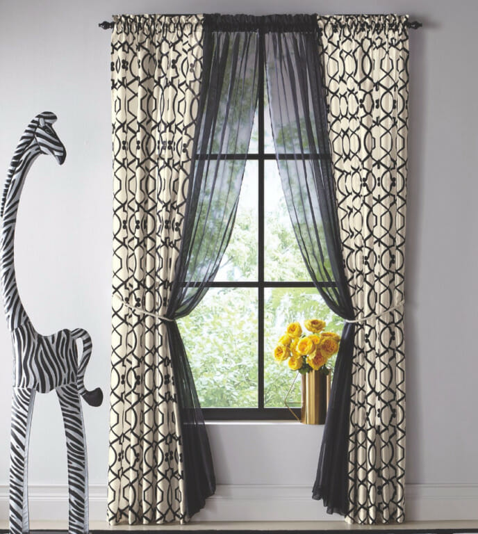 A black and white panel pair with black sheer curtains, vased yellow roses, and a tall giraffe in a zebra stripe finish.