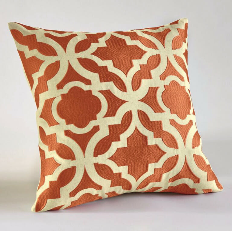 A quilted throw pillow in orange and beige, in a baroque tile pattern.