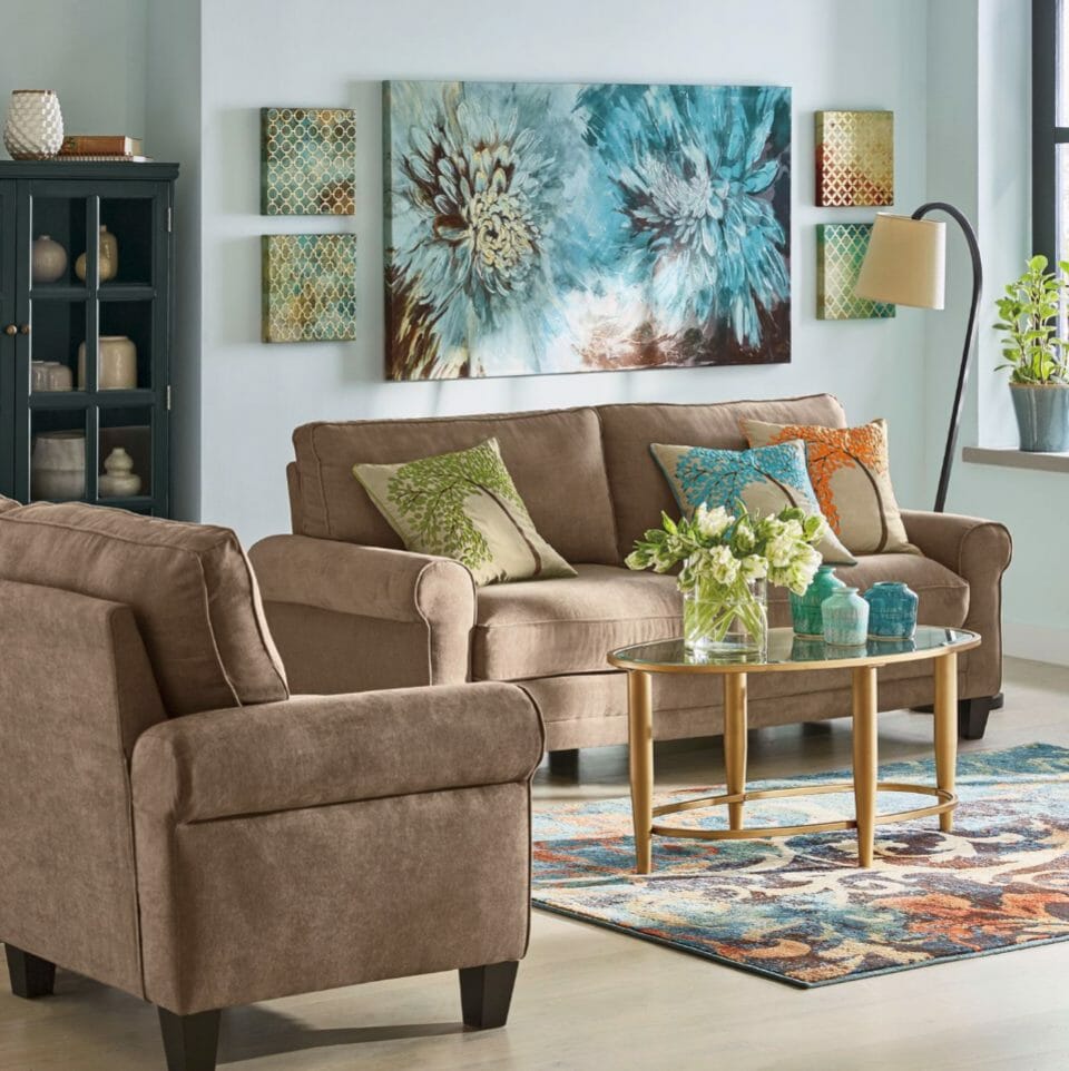 A large wall canvas of two dahlias in turquoise and brown, a tan sofa and chair, toss pillows, and a swirled throw rug. 