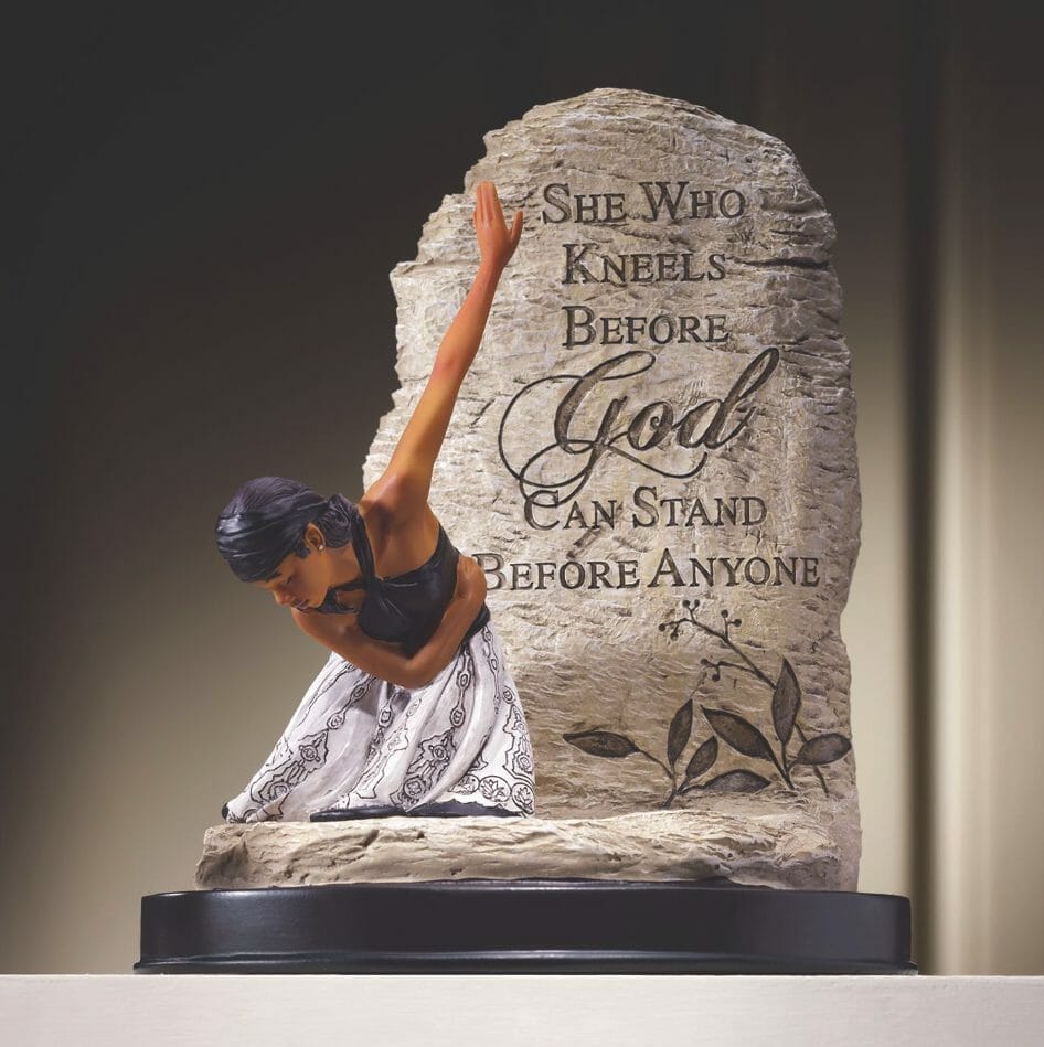 Figurine of a kneeling woman with arm upraised, by a rock inscribed with She Who Kneels Before God Can Stand Before Anyone.