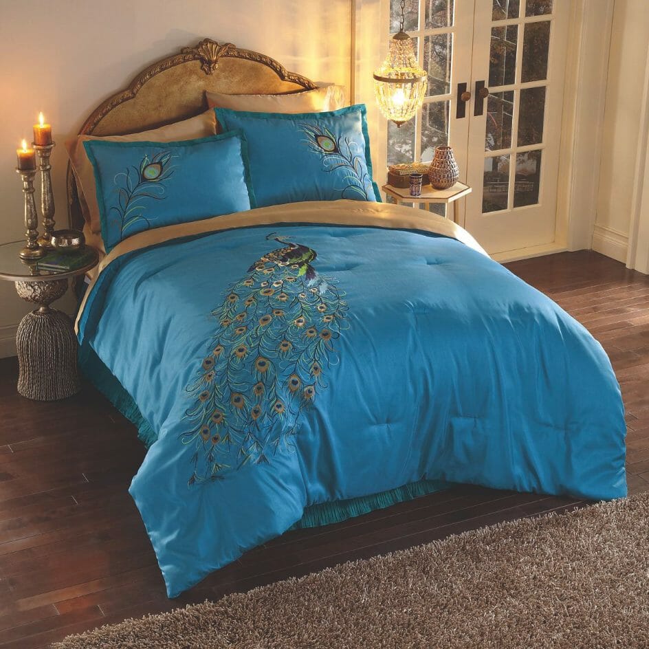 A turquoise bed set with an embroidered peacock, feathers on shams, two lit candles and a small lit chandelier.