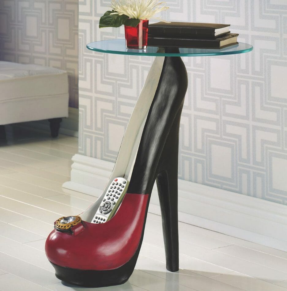 A red and black stiletto heel stand with a round glass top, with room for a couple books, vased flower, and controller.