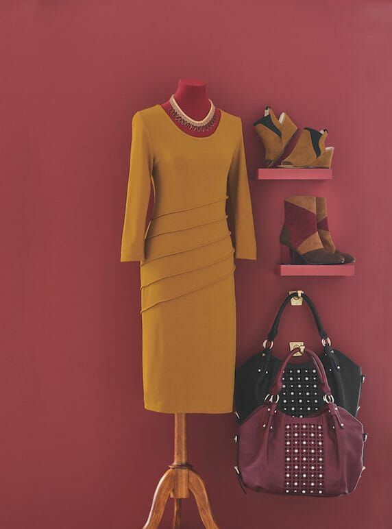 A mustard fitted dress on a mannequin, black and merlot bags, a tan, brown, and merlot bootie, and a tan and black shootie.