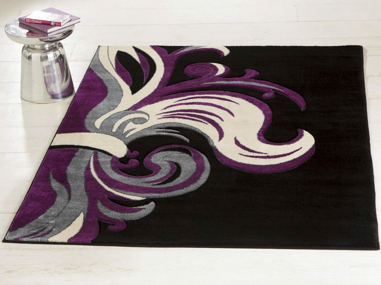 A black area rug with large baroque swirls of white, gray and purple, and purple books on a nearby silver plant stand.