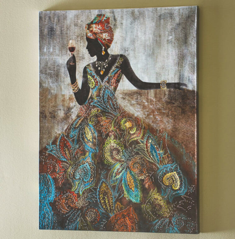 An Afrocentric wall canvas of a black woman holding a wine glass, in a colorful headwrap, full skirted dress, and jewelry.