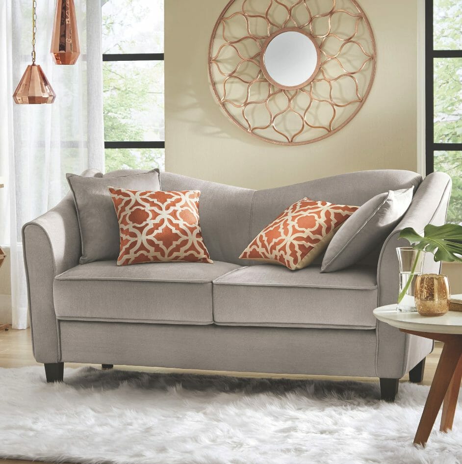 A gray sofa with copper and beige pillows, a large round copper wall mirror, two hanging copper lamps, a white plush rug.
