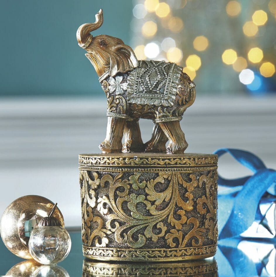 A small, ornate burnished gold oval box, topped by a gold blanketed elephant with a raised trunk.