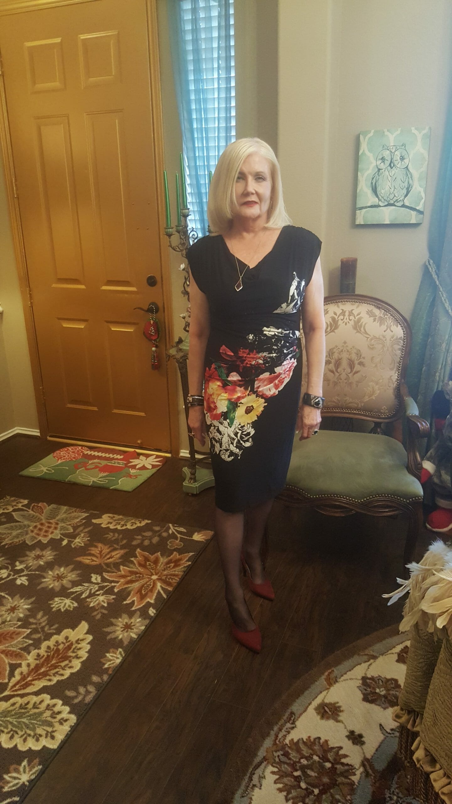 A Midnight Velvet customer in her foyer, in a black V-neck dress with a diagonal splash of white, red and yellow flowers.