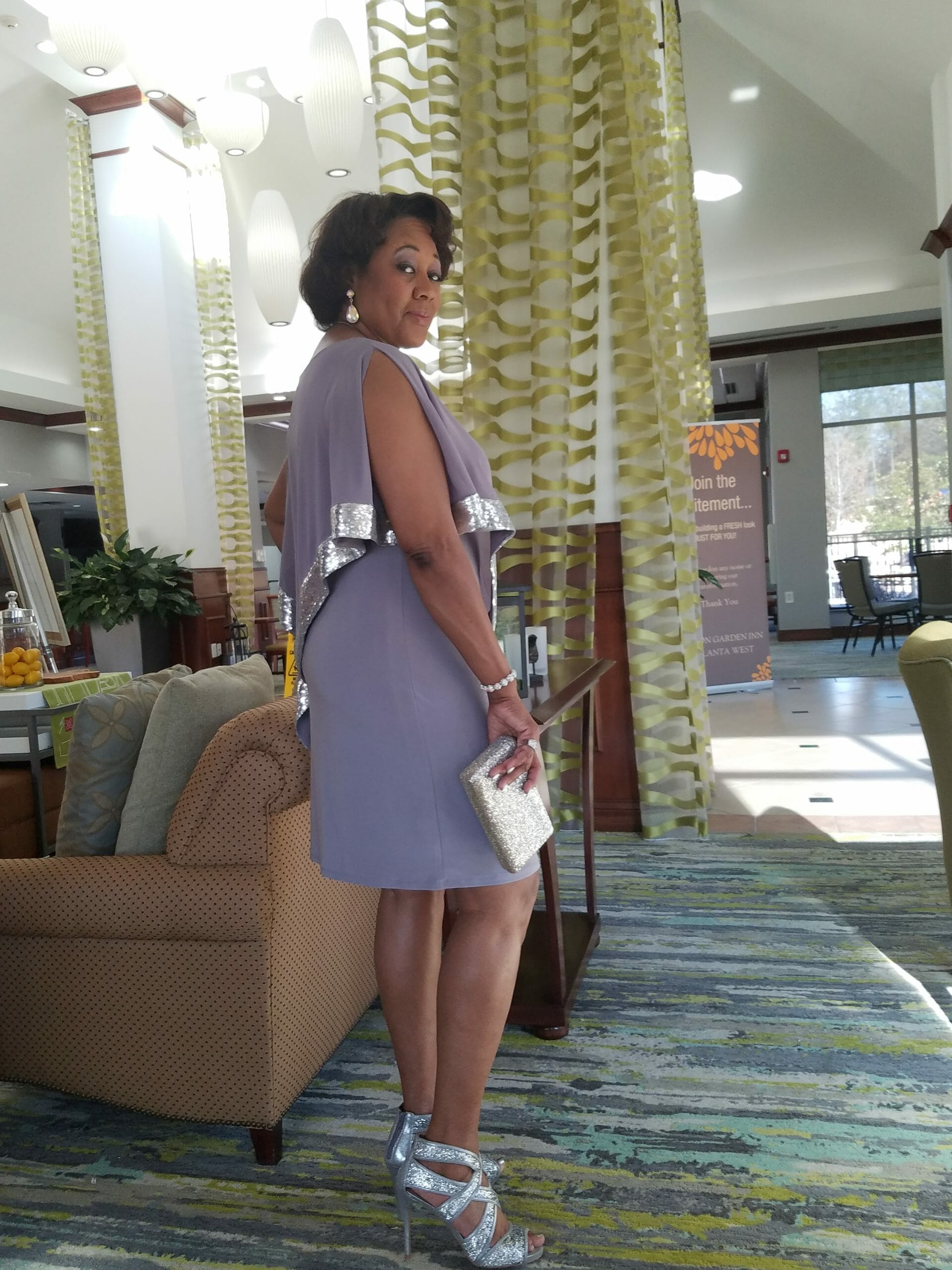 Side view of a Midnight Velvet customer, in a lavender dress with silver trim on the cape-like top, and silver sandals.