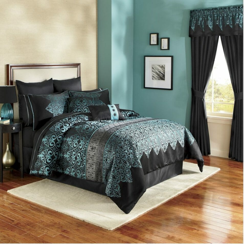 A black and turquoise baroque print bed set with matching curtains, a black nightstand with a turquoise and black lamp.