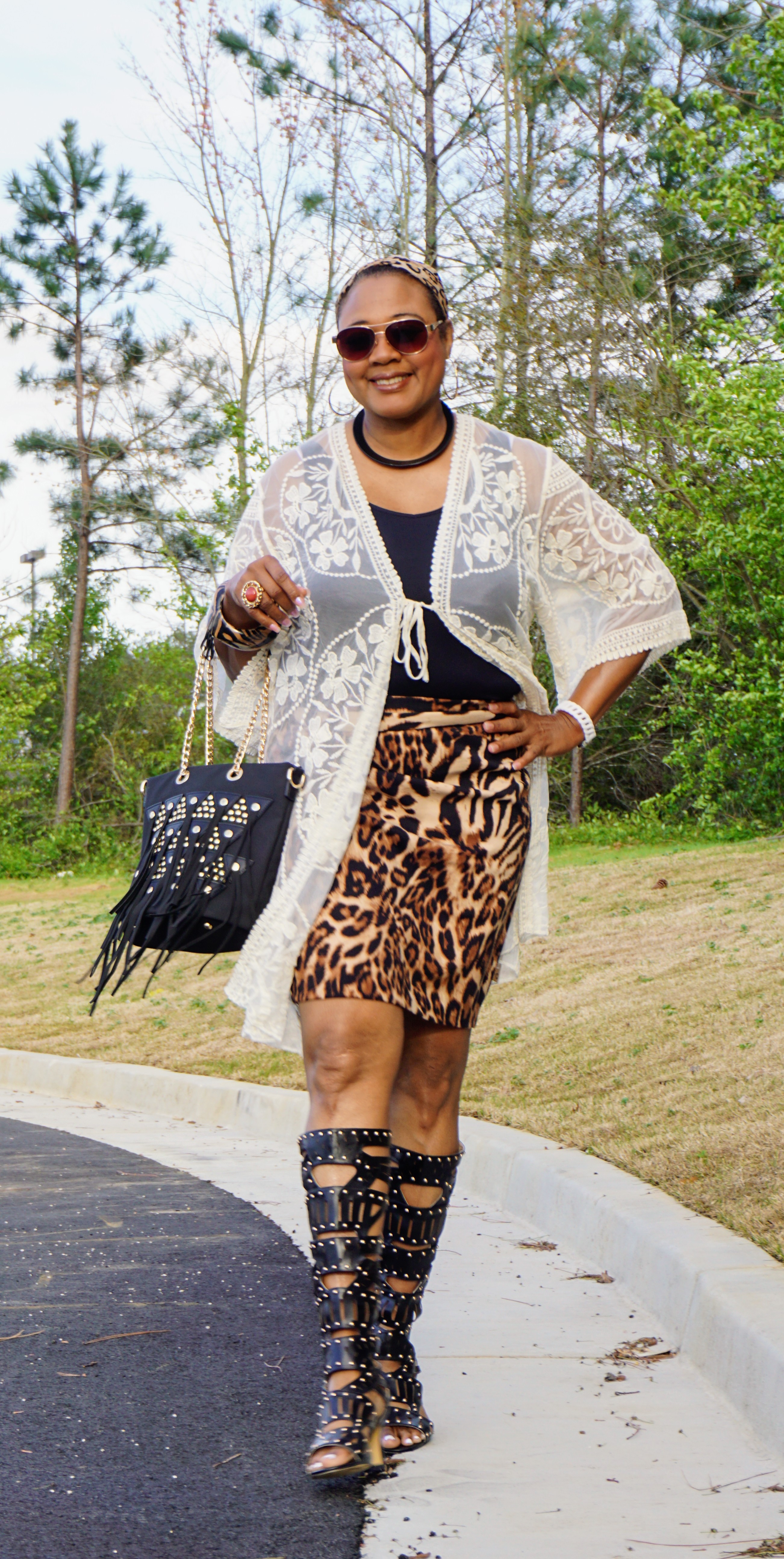 A Midnight Velvet customer in sunglasses, an animal print skirt, black cami, white lace cardigan, and black studded boots.