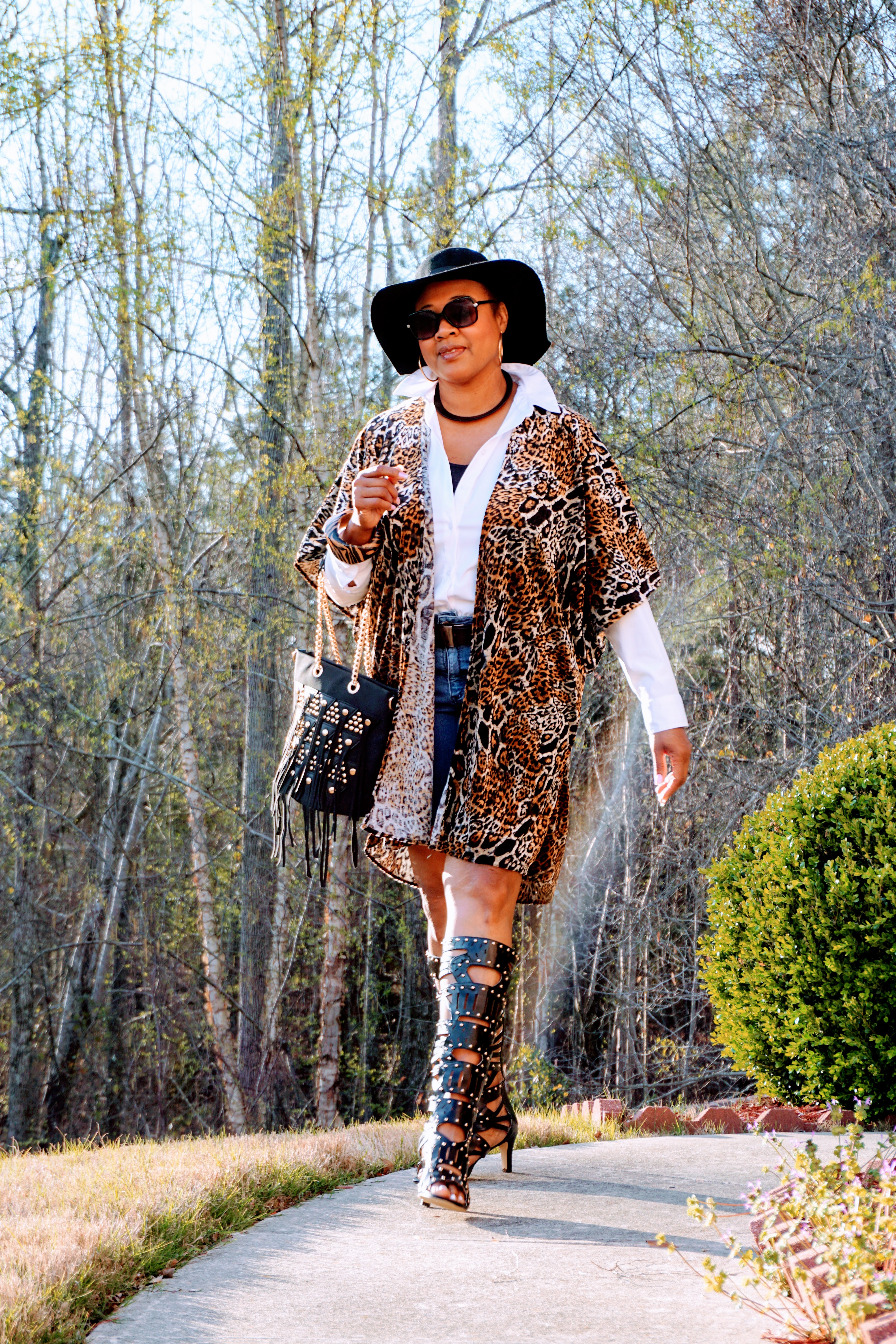 A Midnight Velvet customer in sunglasses, a white shirt, animal print cardigan, black studded boots, and a black hat.